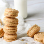 peanut butter macarons stacked and scattered with a bottle of milk