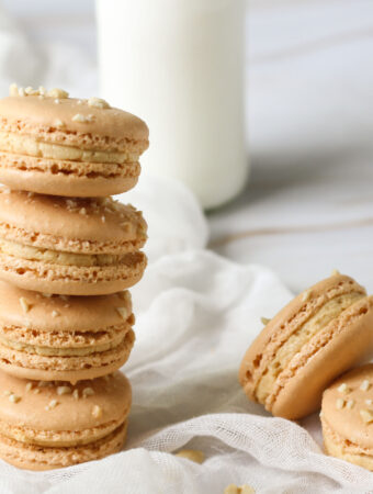 peanut butter macarons stacked and scattered with a bottle of milk