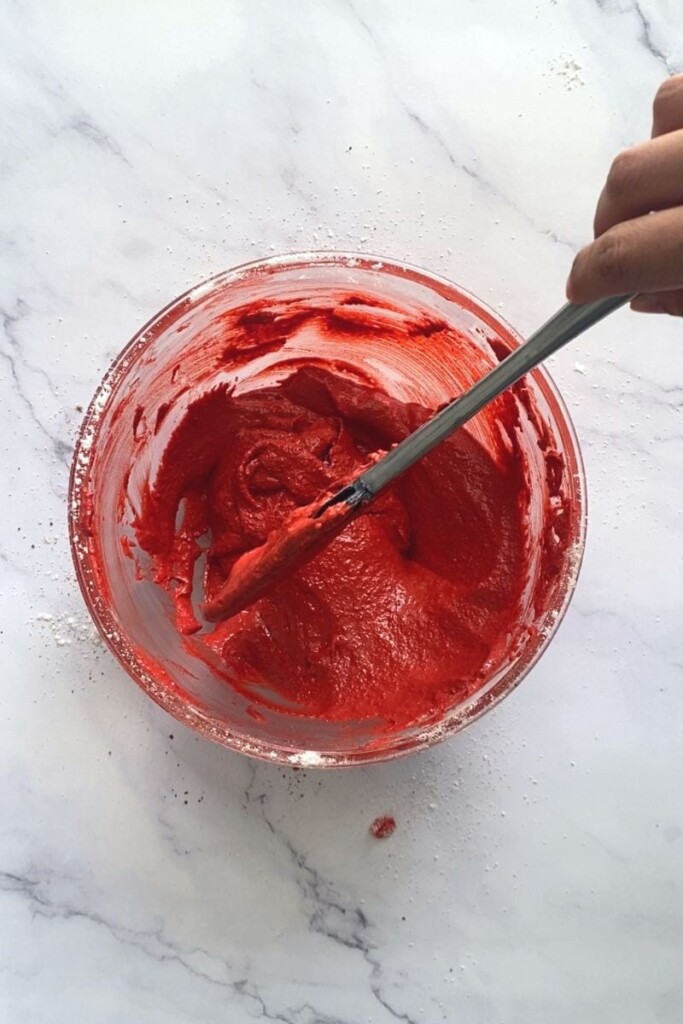 Red velvet macaron batter swirled with spatula.