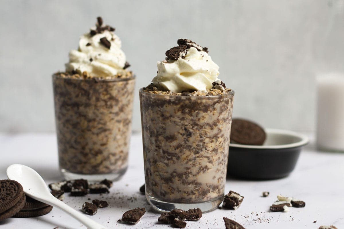 2 glasses of oreo oats topped with cream and crushed cookies.