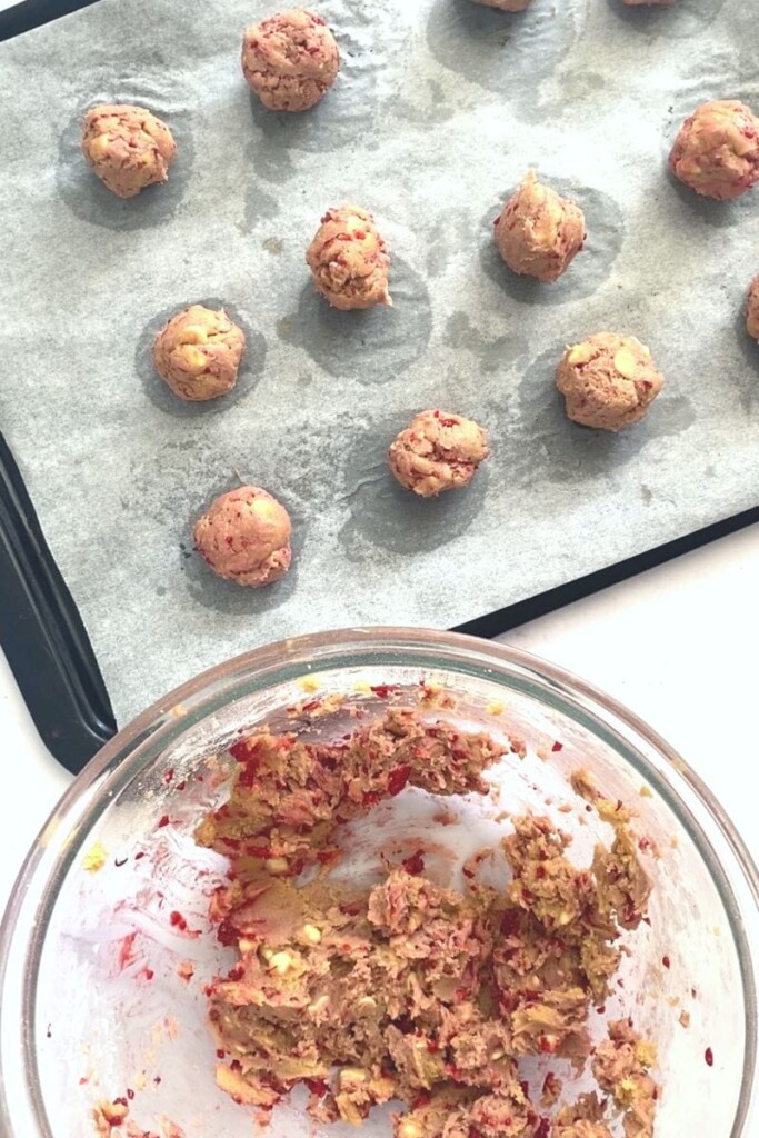 White chocolate and raspberry cookie dough balls being placed on tray.