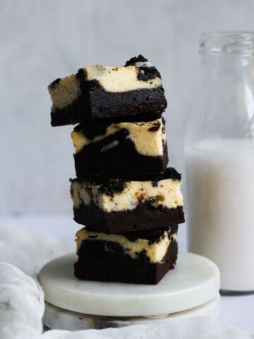 Stacked oreo cheesecake brownies next to a jug of milk.