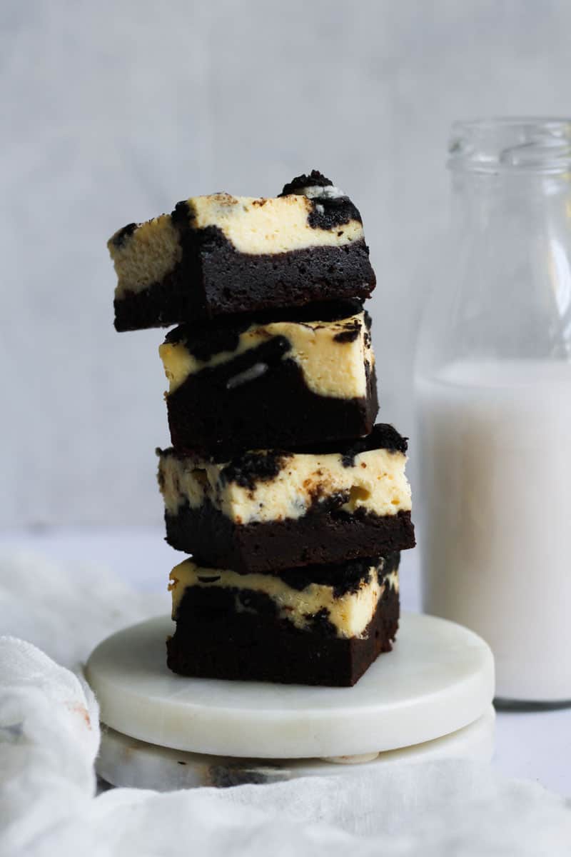 Stacked oreo cheesecake brownies next to a jug of milk.