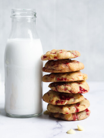 White chocolate and raspberry cookies stacked on the right side of a jug of milk.