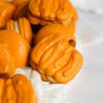Pumpkin shaped macarons laid next to pumpkin spice macarons.