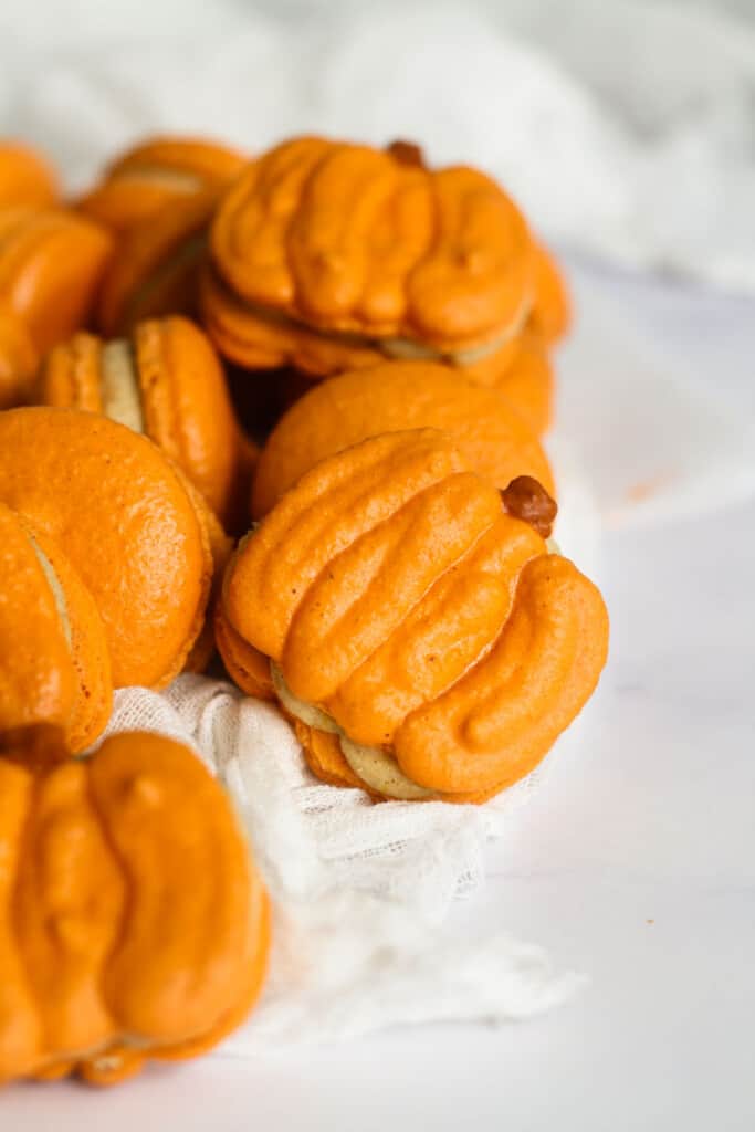 Pumpkin shaped macarons laid next to pumpkin spice macarons.