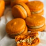 Pumpkin macarons laid on cloth with the a bite out of the one in the front.