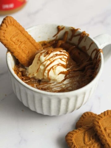 Biscoff mug cake in mug topped with ice cream and biscoff spread.