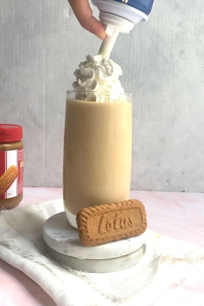 Piping cream on top of biscoff milkshake.