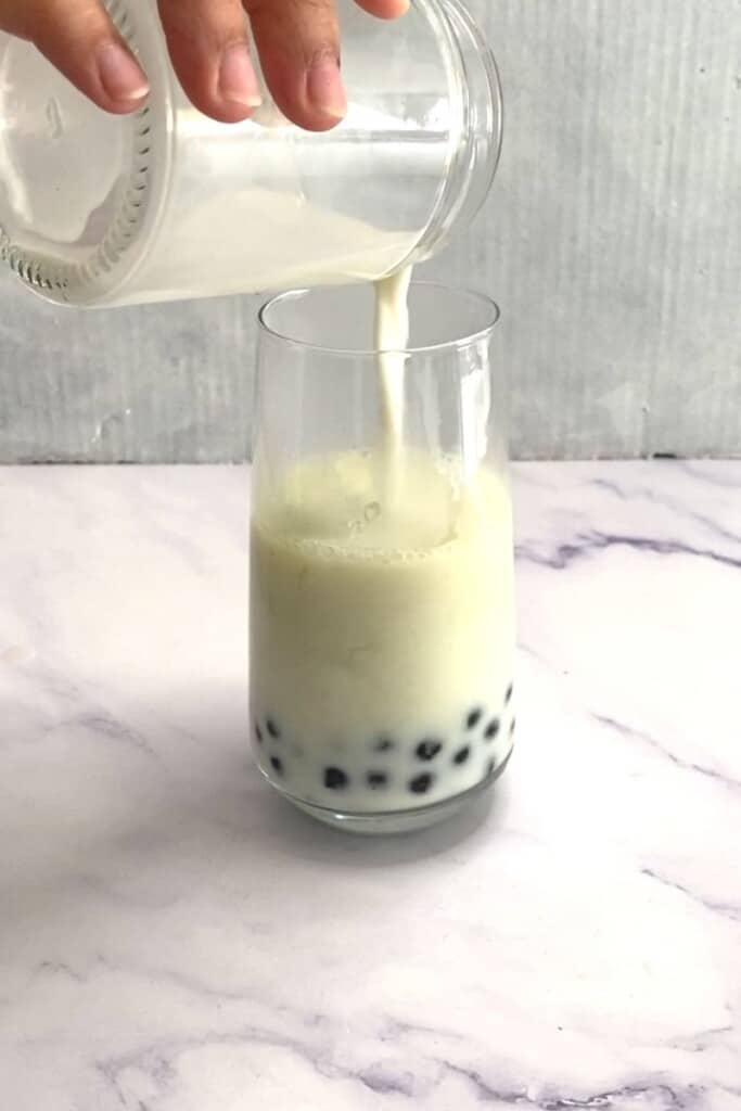 Pouring milk into honeydew boba tea.