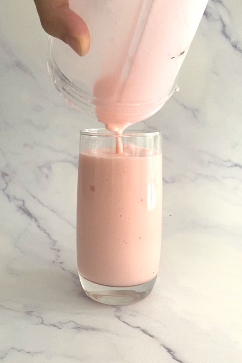 Rose syrup milkshake being poured into tall glass.