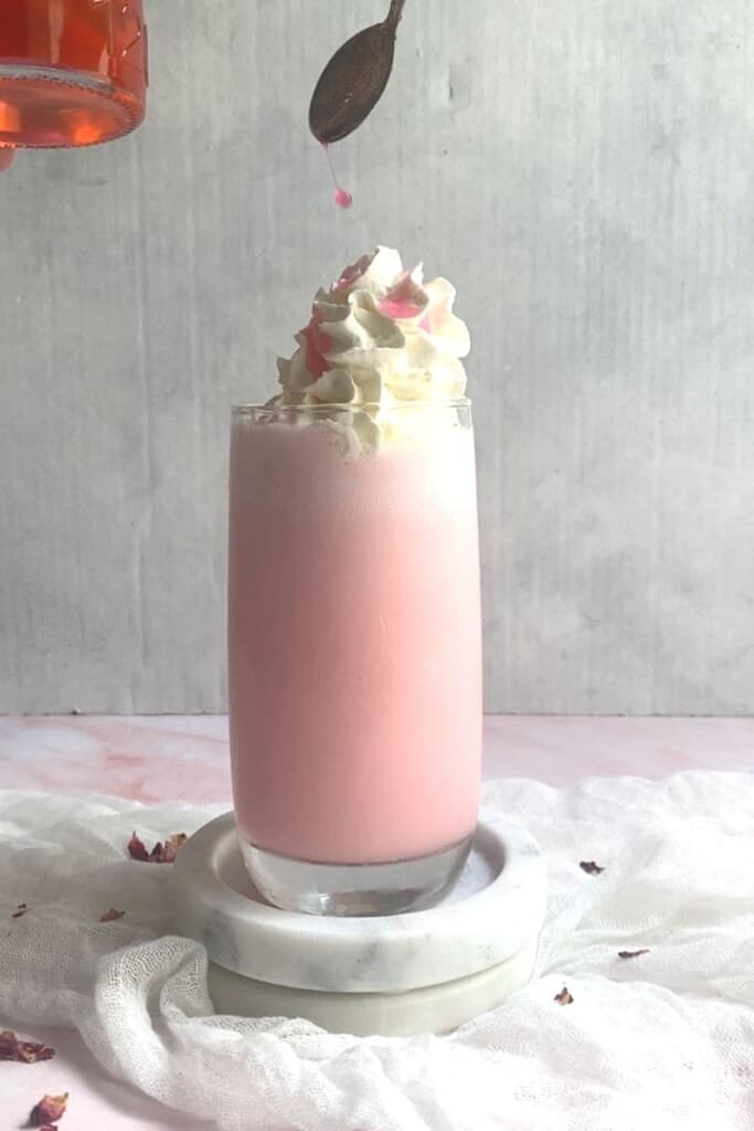 Rose milk shake topped with cream and rose syrup being drizzled.