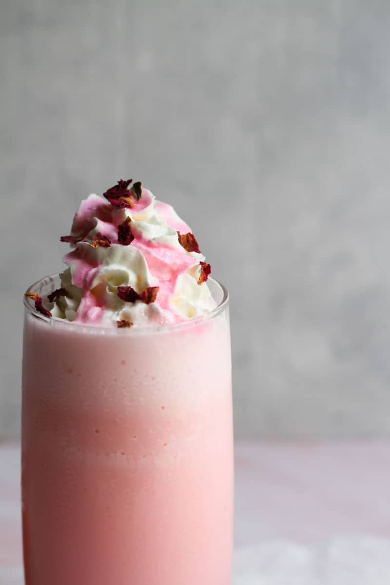 Rose milkshake topped with cream and decorated with rose syrup and rose petals.