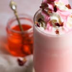 Close up of top of rose milkshake with rose syrup in the background.