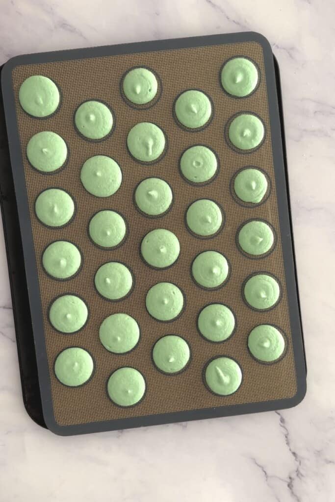 Green macarons piped circles onto a tray.
