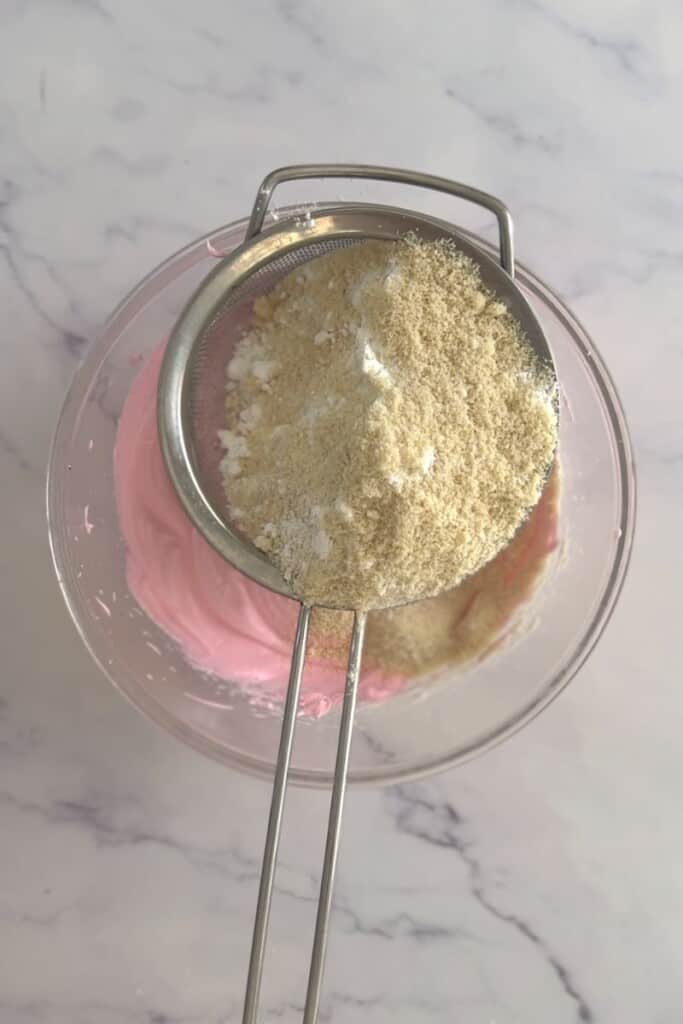 Sifting almond meal and icing sugar into pink meringue.