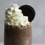 View of top of the glass of Oreo Milkshake without ice cream topped with cream and Oreos.