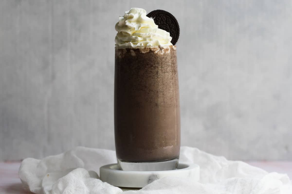 Landscape view of glass of Oreo Milkshake without ice cream topped with cream and Oreos.