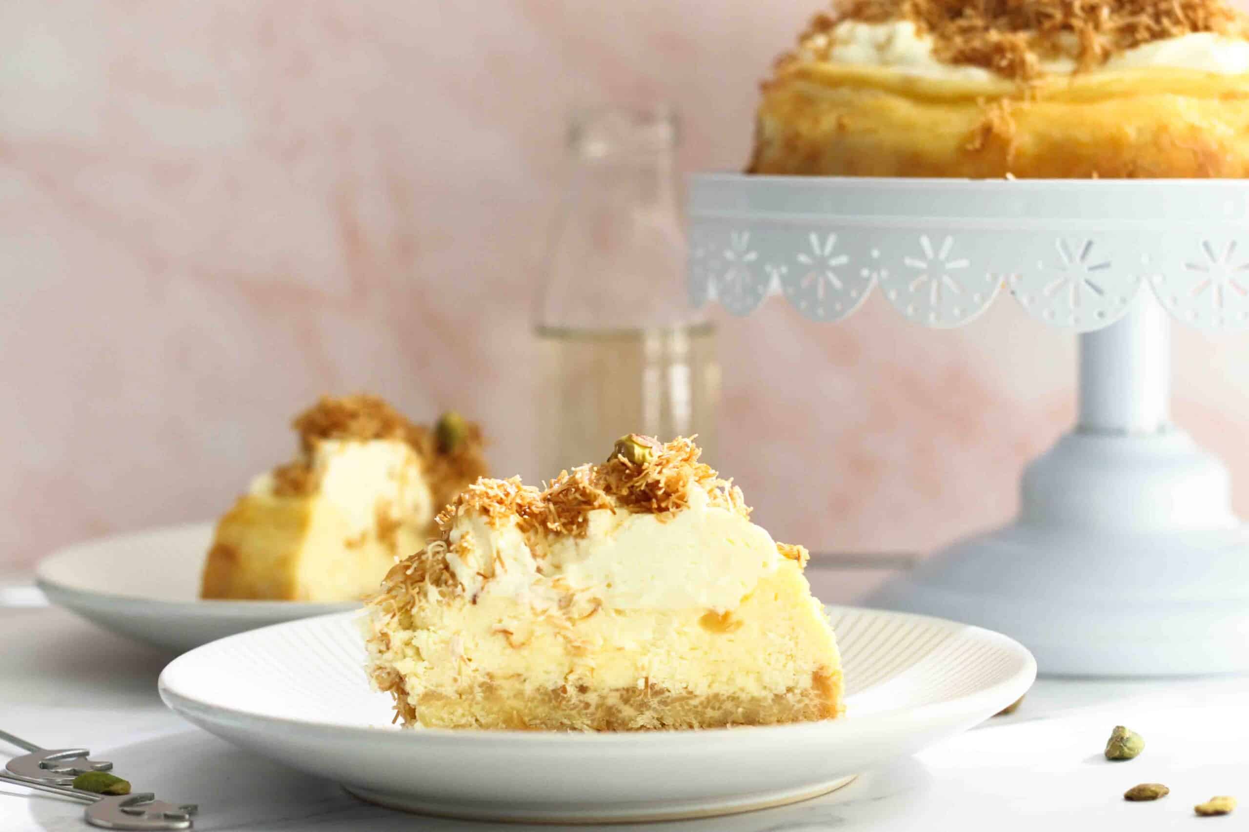 Close up of knafeh cheesecake slice with another slice and the rest of the cheesecake in the background.