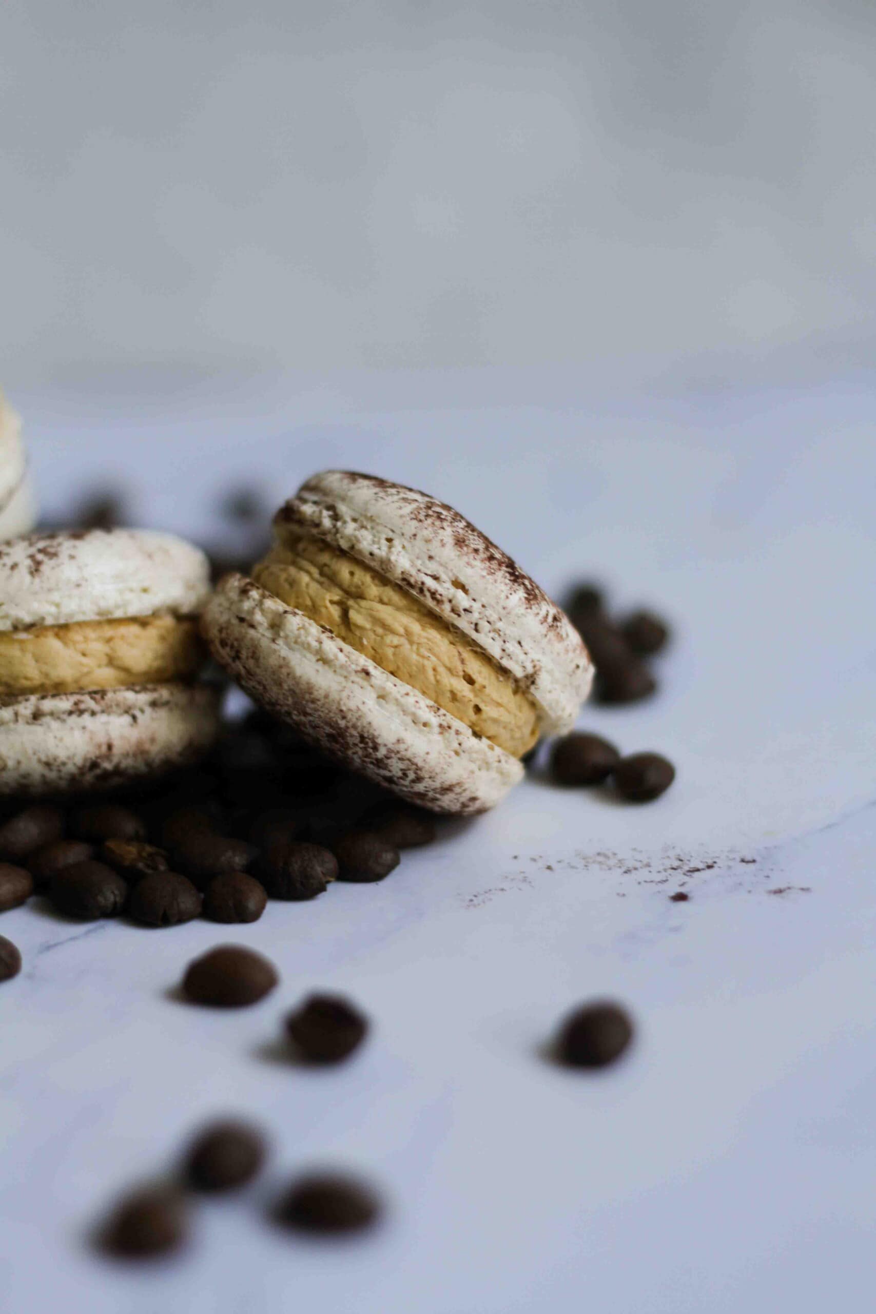 Close up of coffee tiramisu macaron with coffee beans in the foreground.