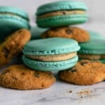Blue macarons with cookie dough buttercream filling sitting on top of chocolate chip cookies.